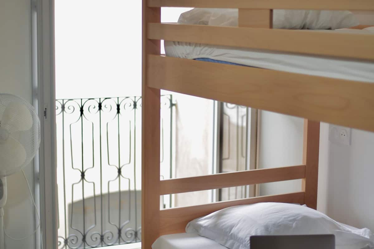 A bunk bed with a laptop on the lower bunk, a fan, and a pair of flip-flops on the floor.