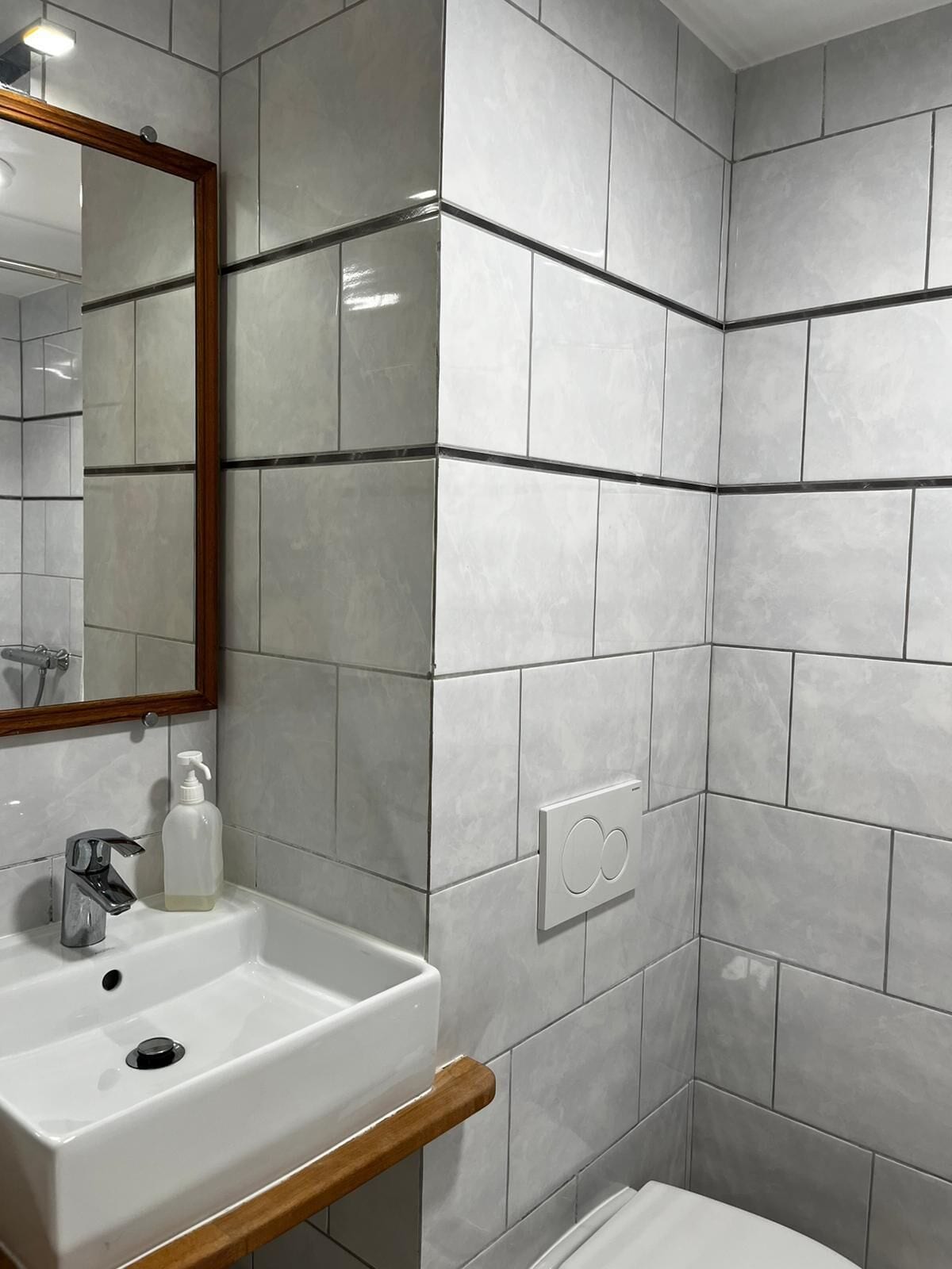 A bathroom with a white sink, a mirror with a wooden frame, and tiled walls.