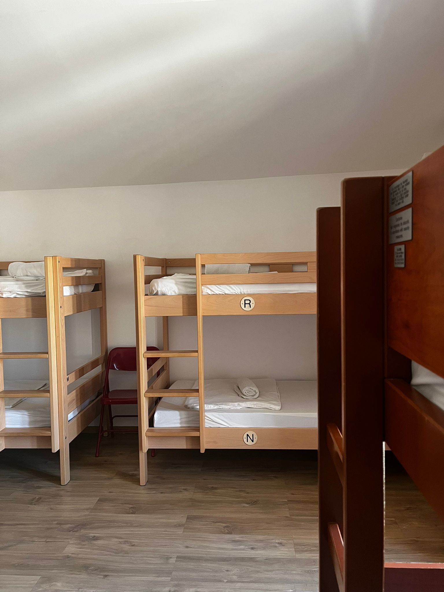 Een slaapzaal met stapelbedden, houten vloeren en een rode stoel.