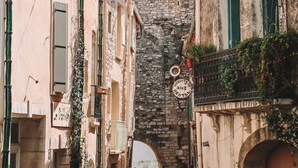 A narrow street with historic buildings, a bell tower, and a stone archway. - Hostel Le Diablotin (Saint-Jean-de-Fos)