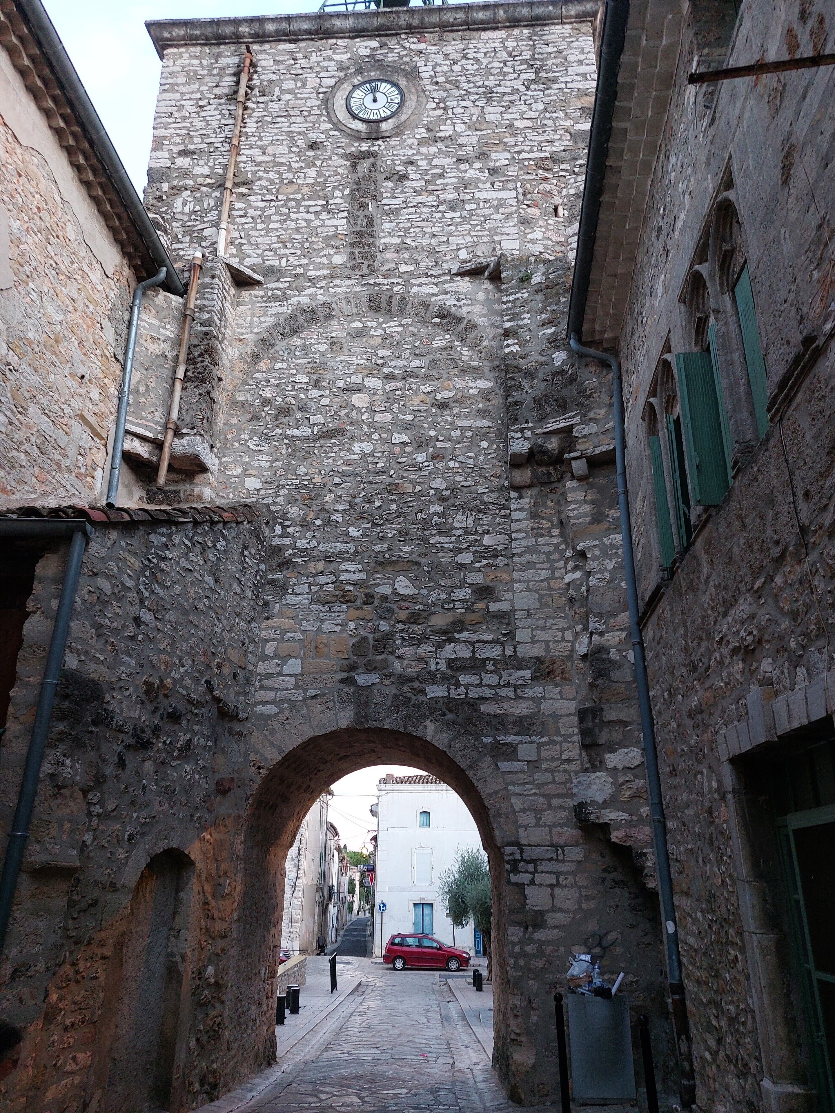 Uma rua estreita com um arco de pedra que dá acesso a um edifício com uma torre do relógio.