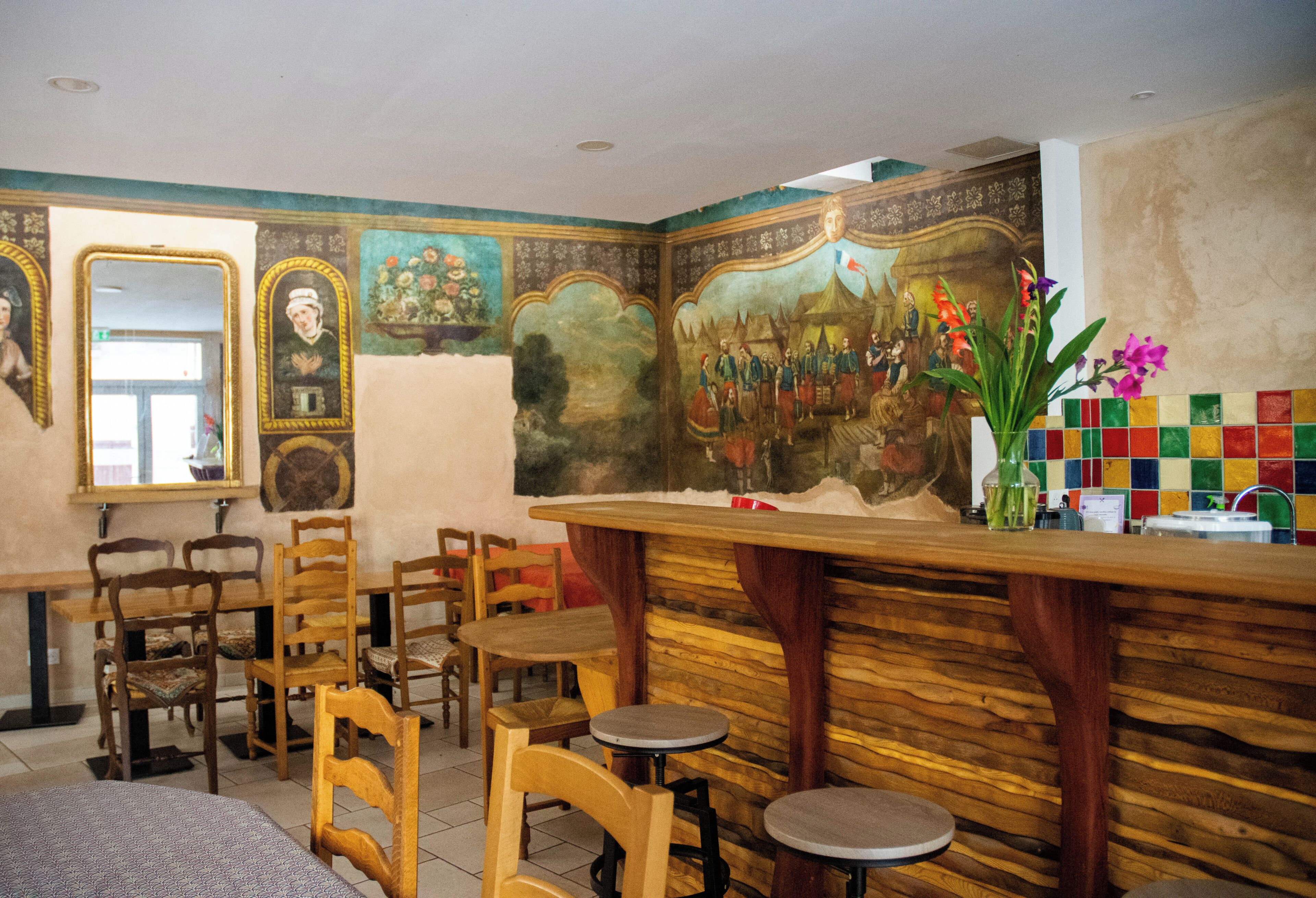 A restaurant interior with wooden chairs, a bar area, and a mural on the wall.