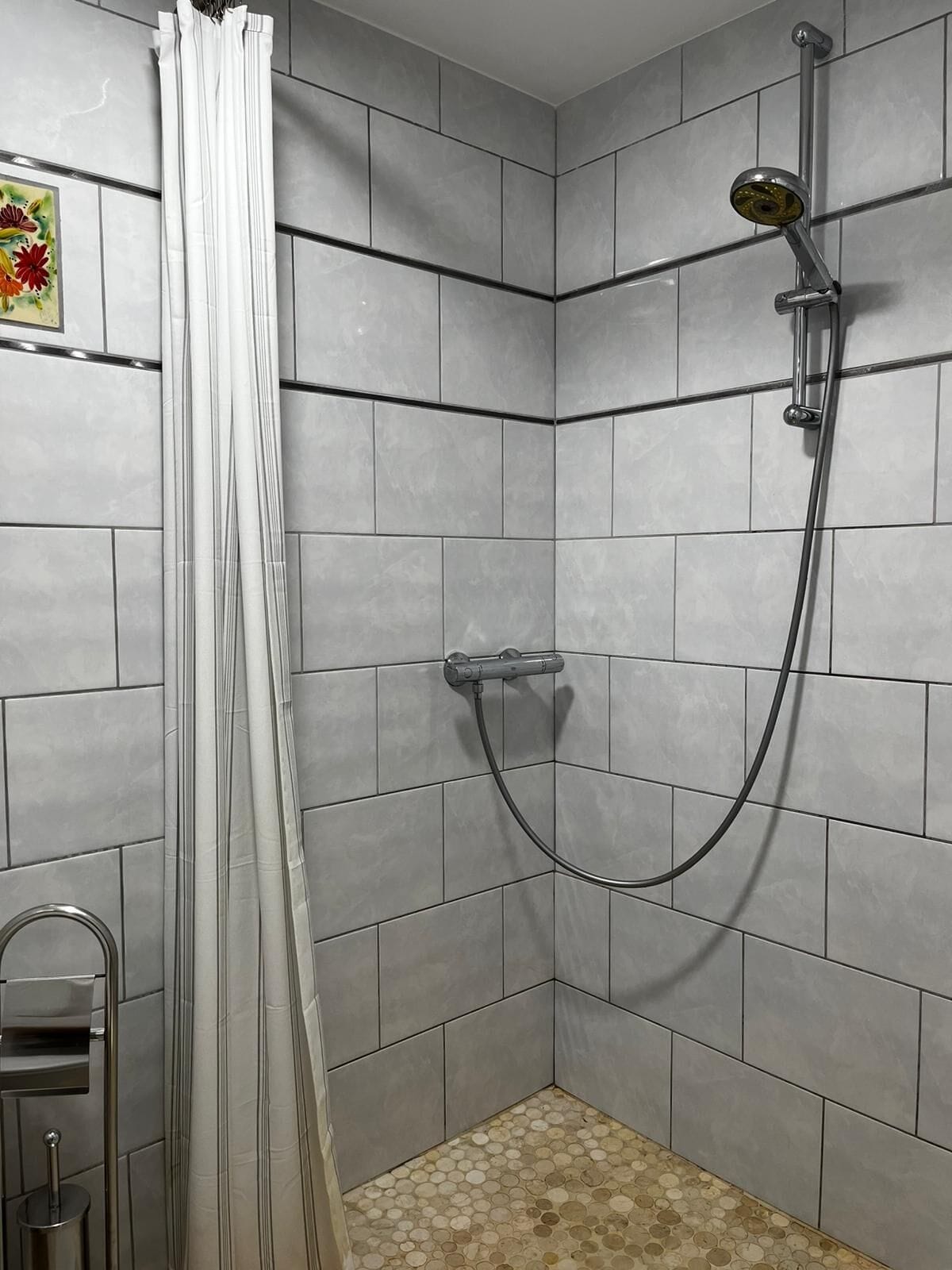 A shower area with a showerhead, curtain, and tiled walls.