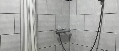 A shower area with a showerhead, curtain, and tiled walls.