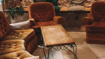 Una habitación con paredes de piedra, un cuadro grande de paisaje, y un rincón de estar con sillones de terciopelo y una mesa de centro de madera.