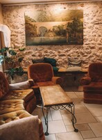Una habitación con paredes de piedra, un cuadro grande de paisaje, y un rincón de estar con sillones de terciopelo y una mesa de centro de madera.