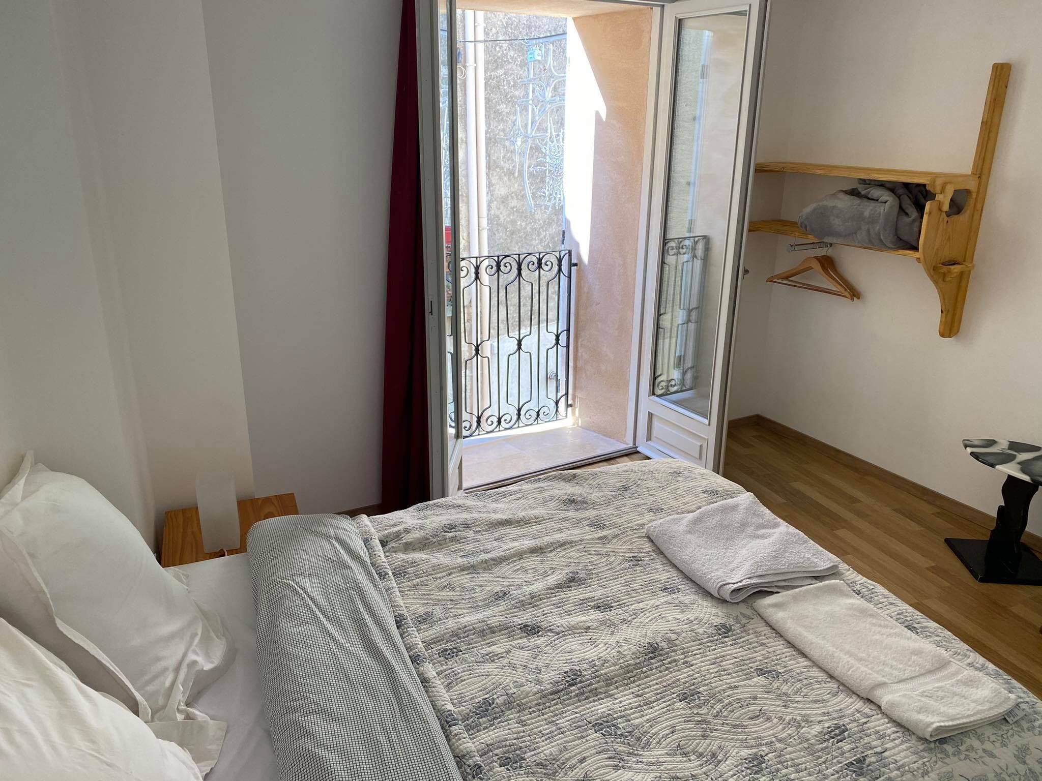 Een slaapkamer met een bed, een houten vloer, een raam met een metalen hekwerk en een houten plank met kleding.