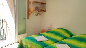 A room with two beds, a wooden shelf, a door, and a view of the outside. - Hostel Le Diablotin (Saint-Jean-de-Fos)