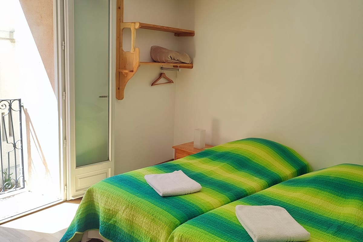 A room with two beds, a wooden shelf, a door, and a view of the outside.