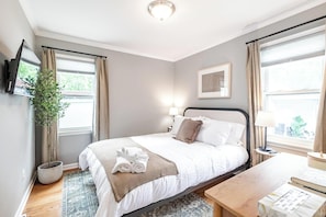 A hotel room with a bed, bedside table, lamp, TV, and a potted plant.
