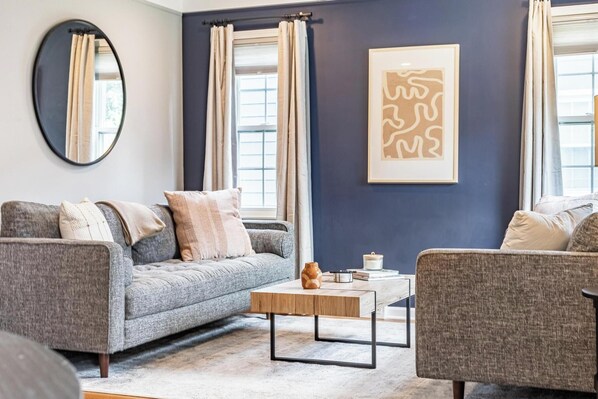 A modern living room with a grey sofa, a matching armchair, a coffee table, and a large mirror.