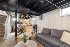 A room with a gray sofa, a round coffee table with a plant, a staircase, and a dining area with chairs and a table.