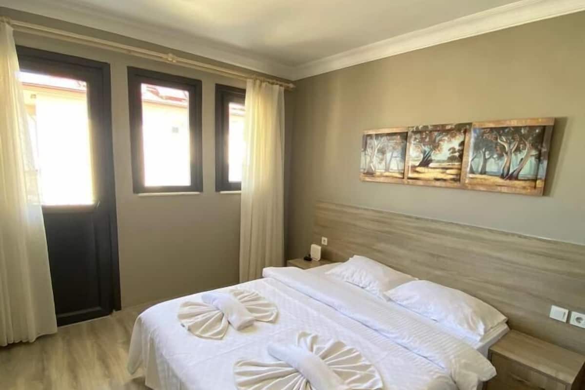 A hotel room with a large bed, a nightstand, and three paintings on the wall.
