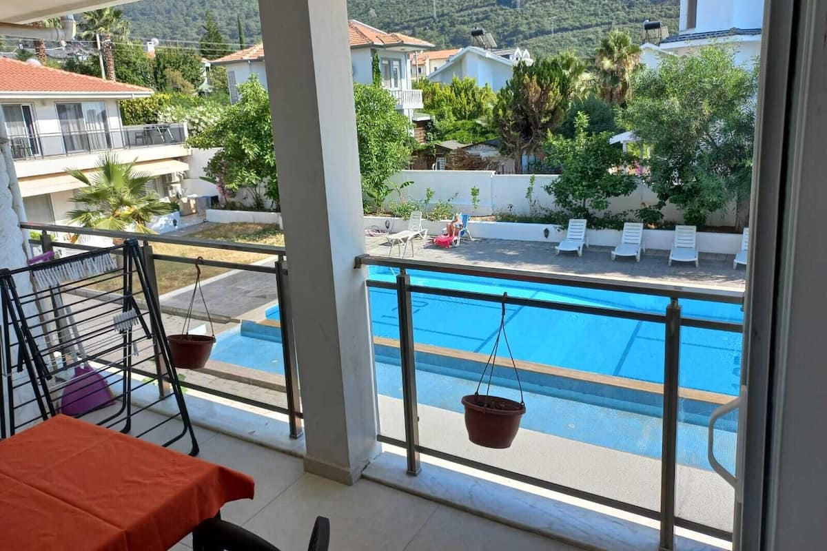 A balcony with a view of a swimming pool, outdoor furniture, and a mountain backdrop.