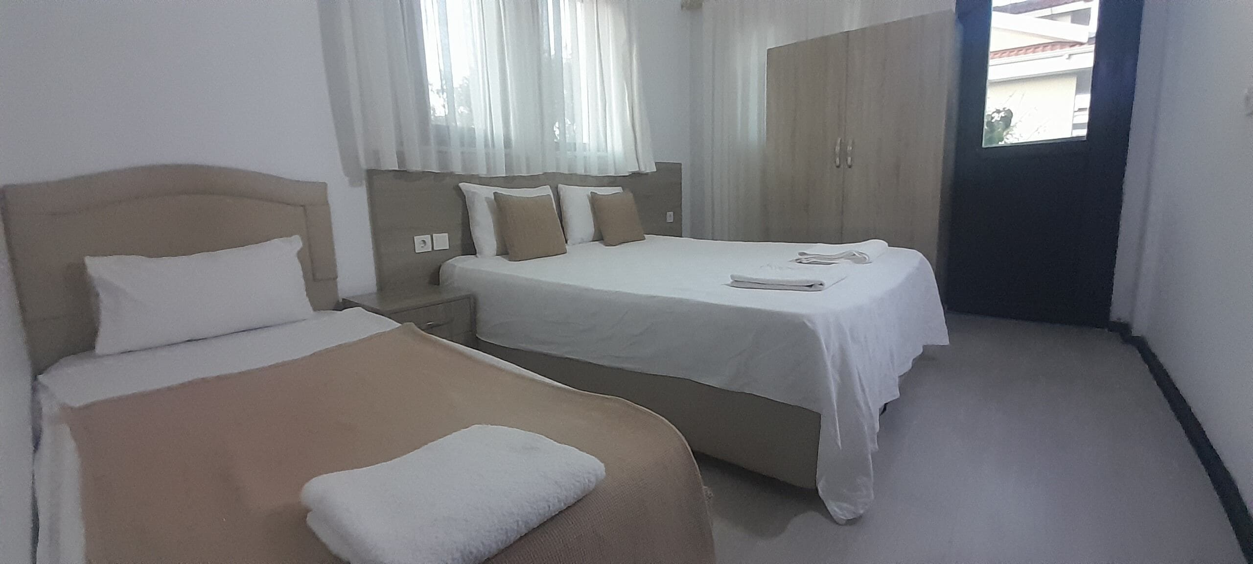 Een hotelkamer met twee bedden, een kledingkast en een raam met gordijnen.