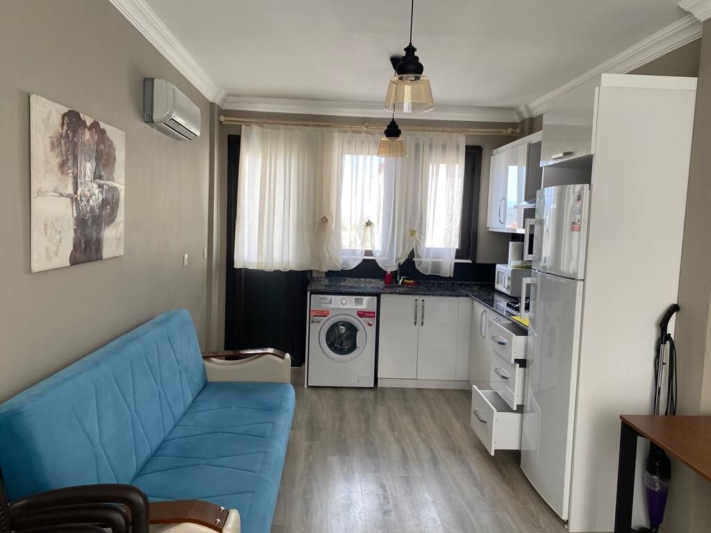 Um espaço compacto com cozinha compacta, máquina de lavar, sofá azul e mesa de jantar.