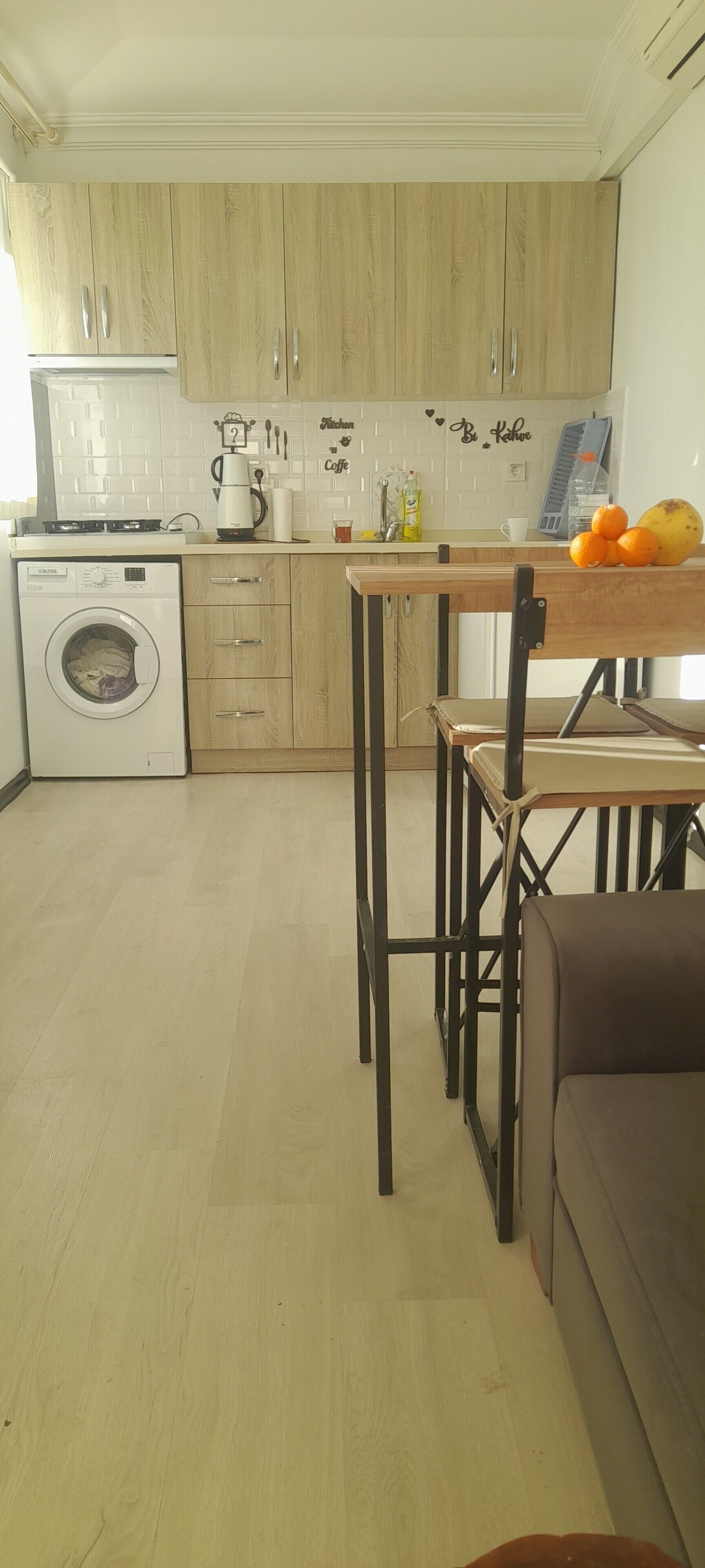 A compact kitchen with wooden cabinets, a washing machine, a table with chairs, and a sofa.