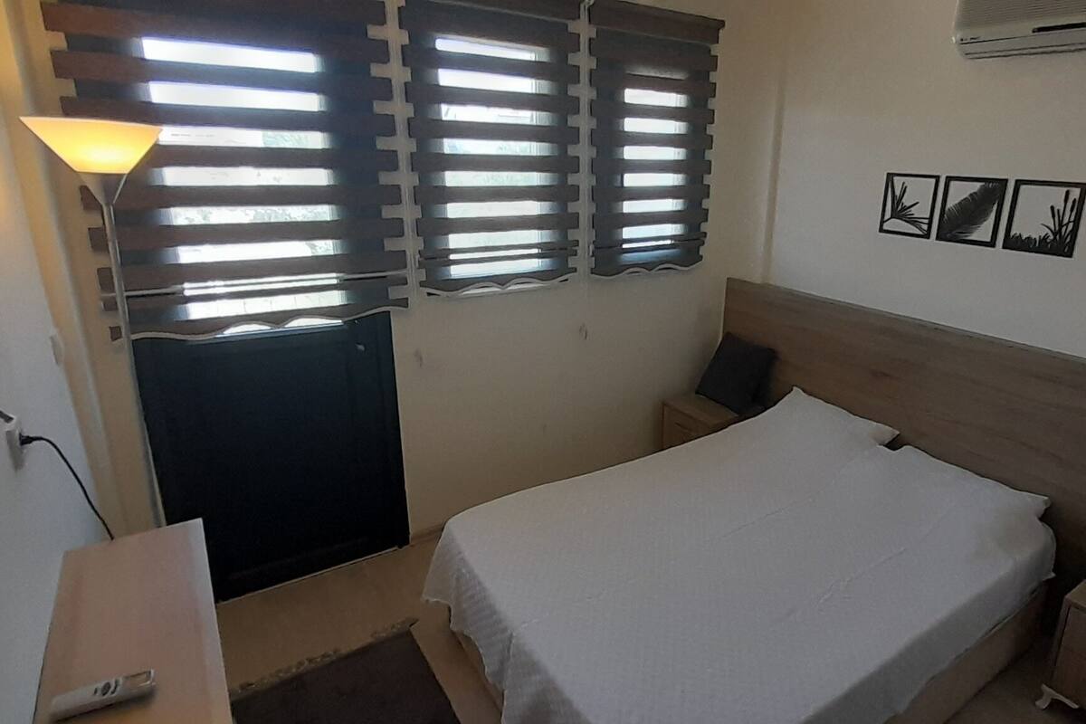 A bedroom with a bed, bedside tables, a lamp, a wall-mounted air conditioner, and a door.