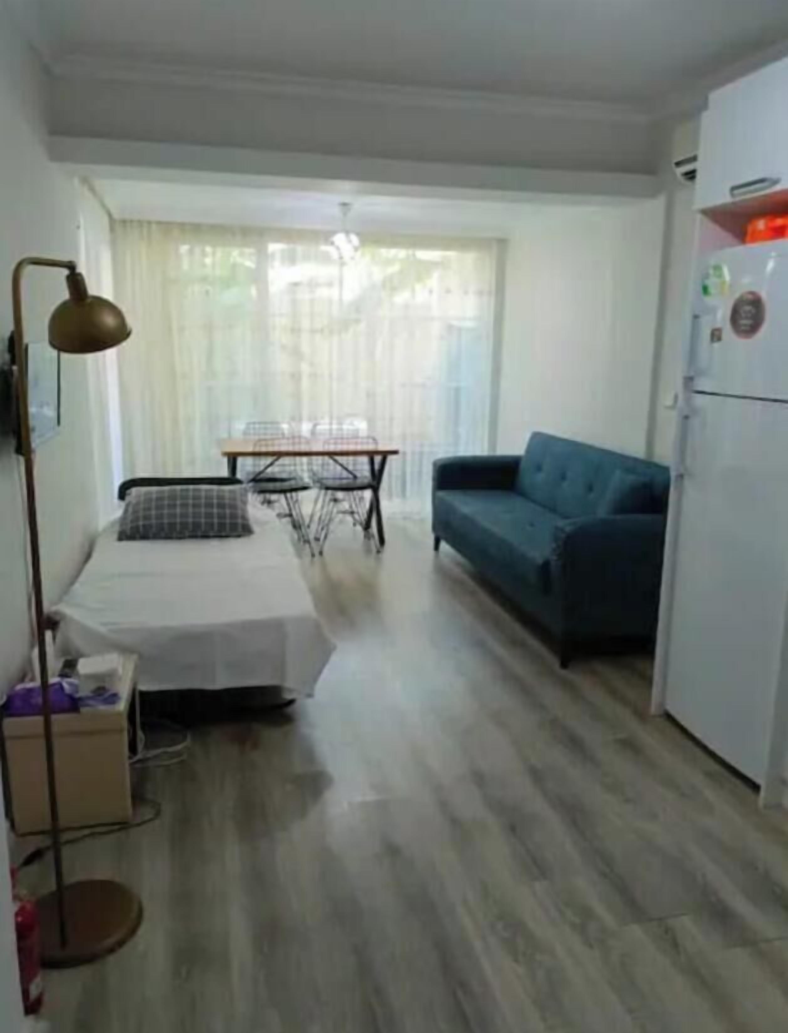 A compact room with a bed, a small table, a sofa, and a refrigerator.