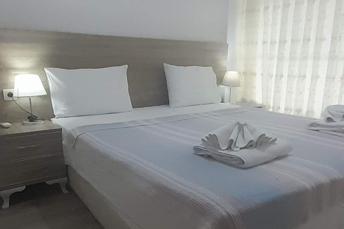 A hotel room with a large bed, a nightstand, a lamp, and an air conditioning unit.