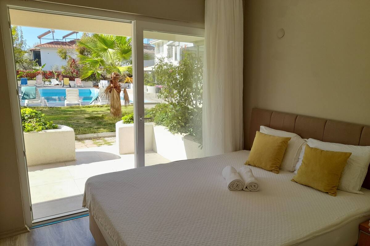 A hotel room with a large bed, a view of a pool and outdoor area, and a sliding glass door.