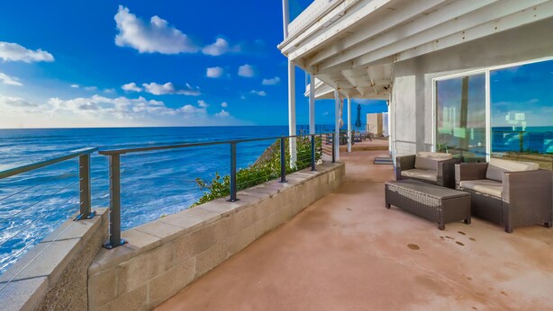 A coastal balcony with outdoor furniture and a view of the ocean.