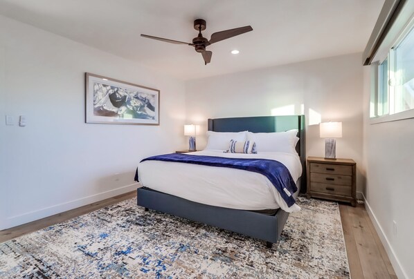 A bedroom with a bed, a ceiling fan, a nightstand, a lamp, and a framed picture on the wall. - Oceanfront Beach Villa With Spectacular Views And Large Private Oceanfront Patio (San Diego)