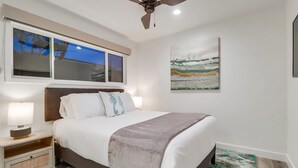 A bedroom with a bed, nightstands, a ceiling fan, a window, and a painting.