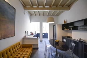 A modern kitchen with a dining area, featuring a yellow sofa, clear chairs, and a marble table.