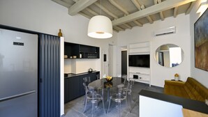 A modern kitchen with a dining area, featuring a large island, clear chairs, and a central light fixture. - Sistina36 Spanish Steps Apartment (Roma)
