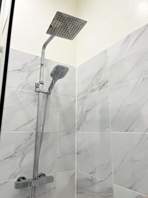 Ducha con cabezal de ducha de mano y cabezal de ducha fijo en un baño con azulejos de mármol.