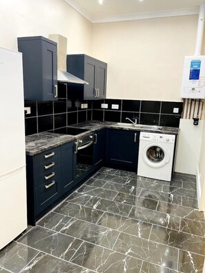 Una cocina compacta con armarios oscuros, horno empotrado, lavadora y salpicadero de azulejos.