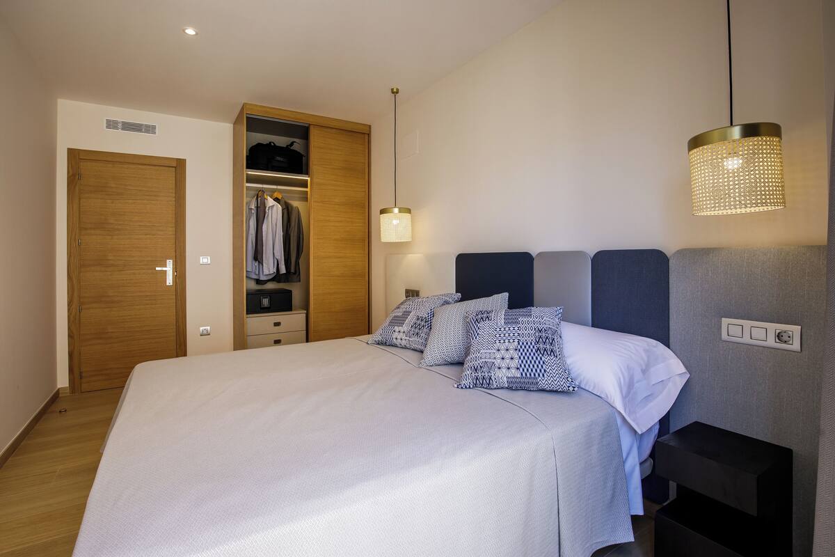 Een slaapkamer met een bed, een kledingkast, een nachtkastje en een hanglamp.