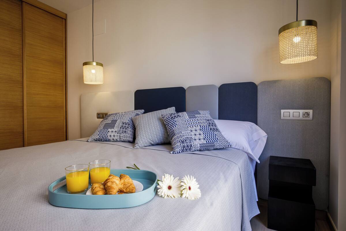 Een netjes opgemaakt bed met gestreepte kussens, een nachtkastje en een dienblad met croissants en sap.