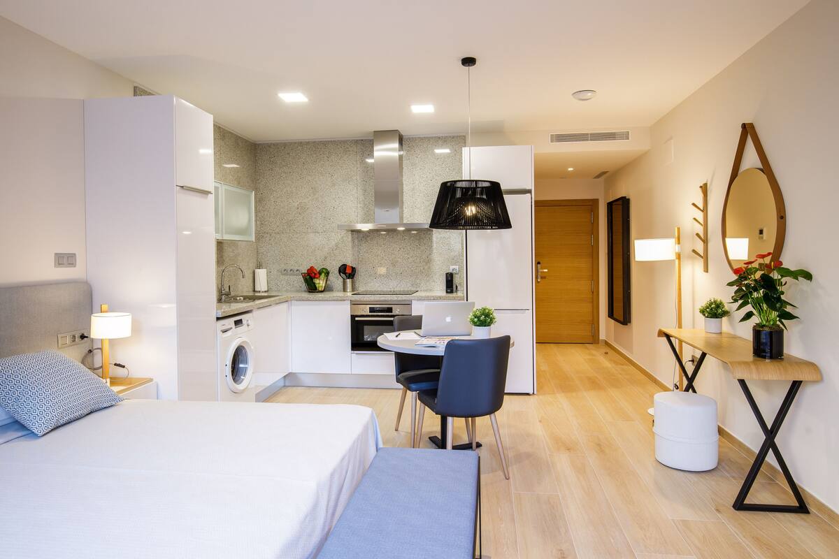 Een moderne hotelkamer met een bed, bureau, stoel, wasmachine en kitchenette.