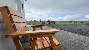Una panchina di legno di fronte a un edificio con un'area pavimentata e un trattore sullo sfondo.