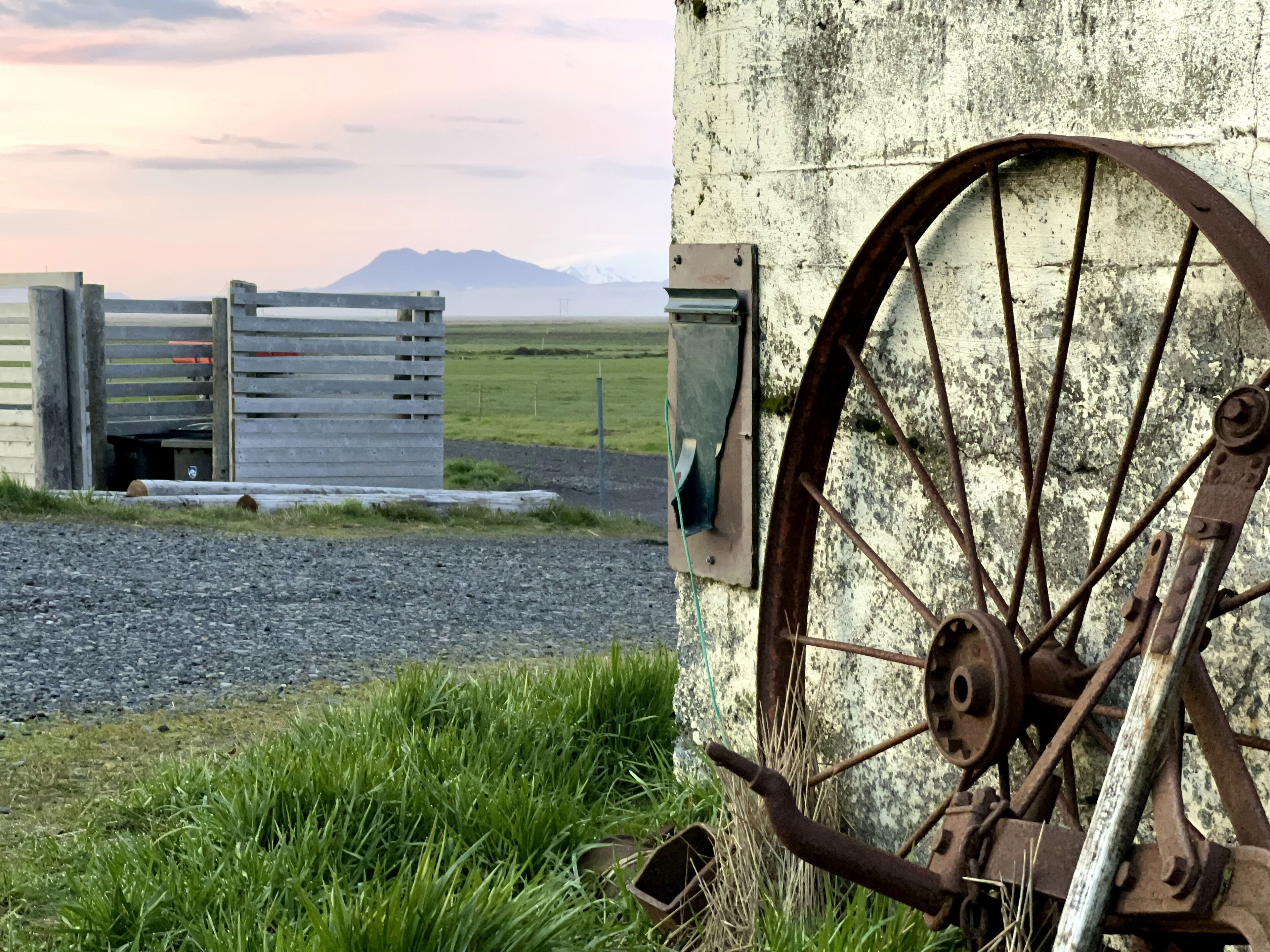 A rustic gate with a metal wheel and a wooden structure in the background.