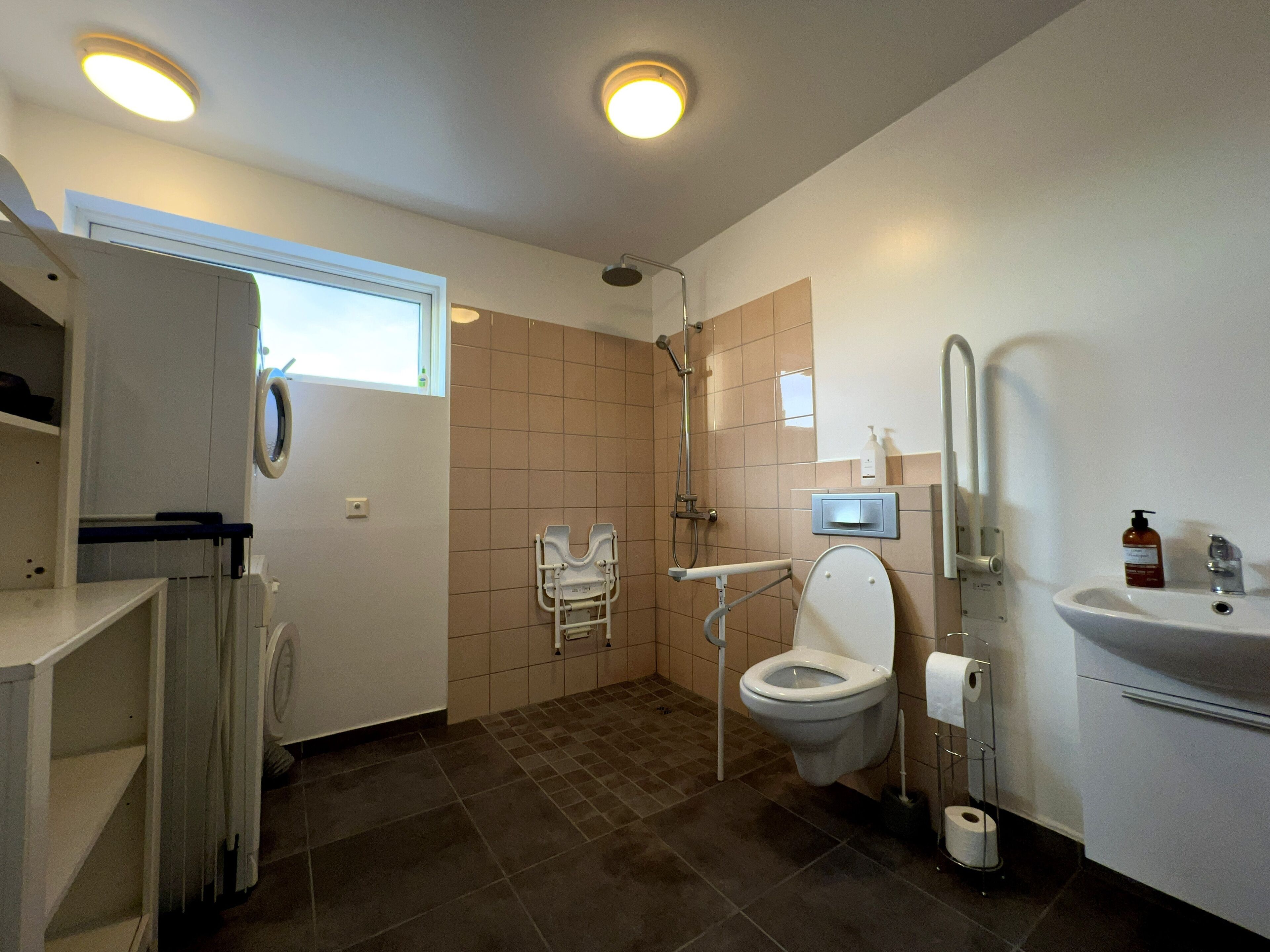 A bathroom with a toilet, sink, shower, and a wheelchair-accessible bench.