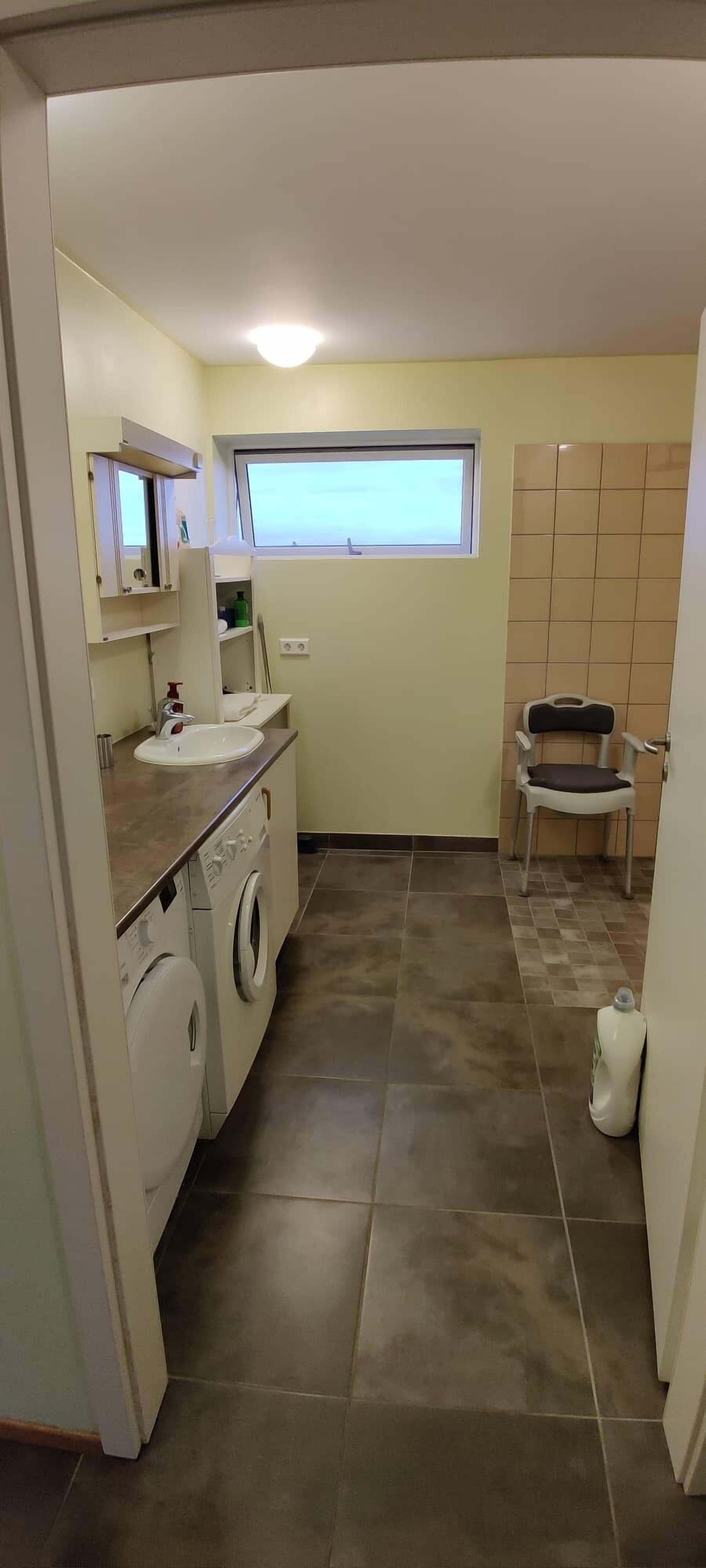 A compact laundry room with a washing machine, a sink, and a chair.