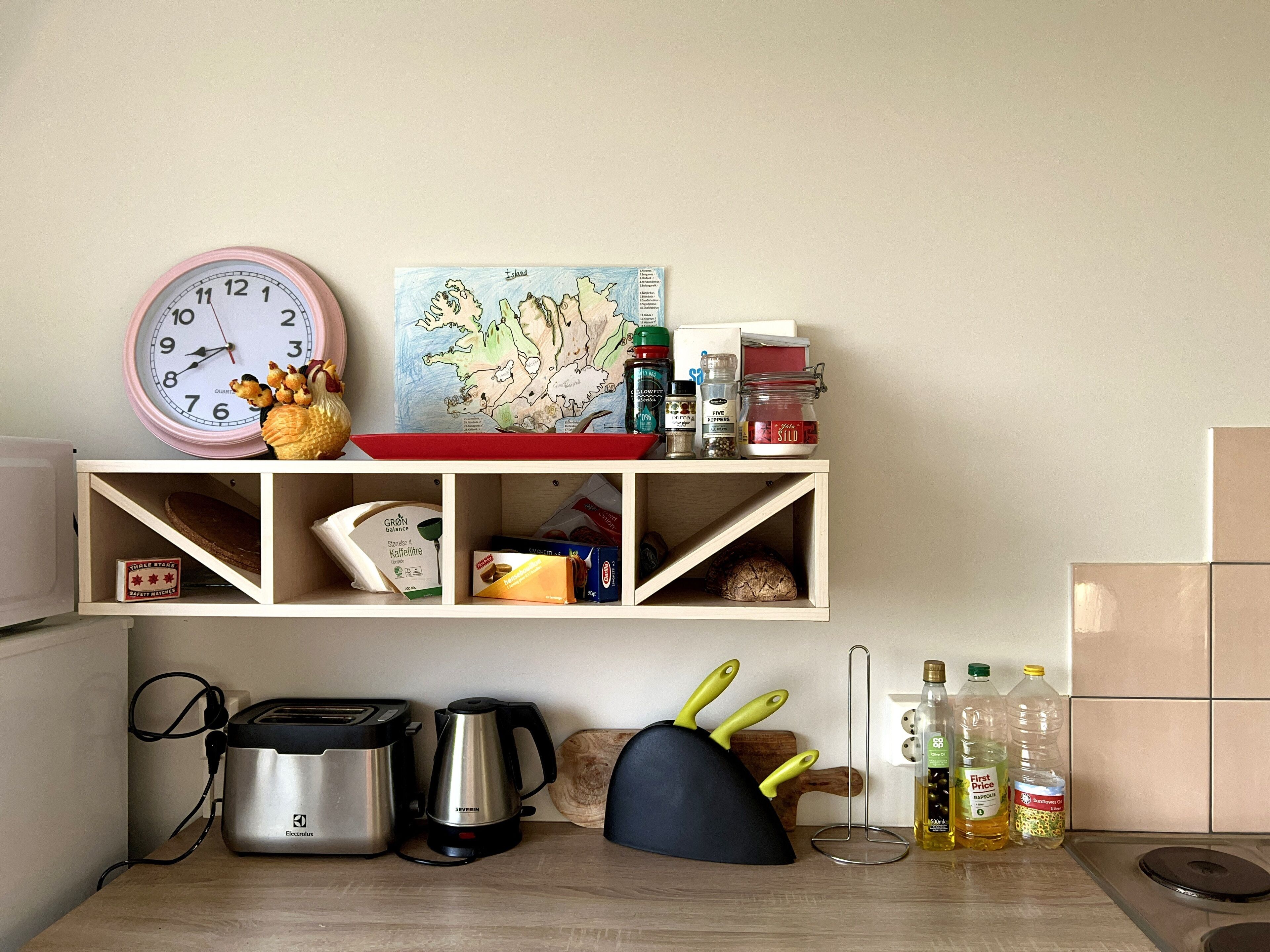 A kitchen with a clock, a map, and various kitchen items on shelves.