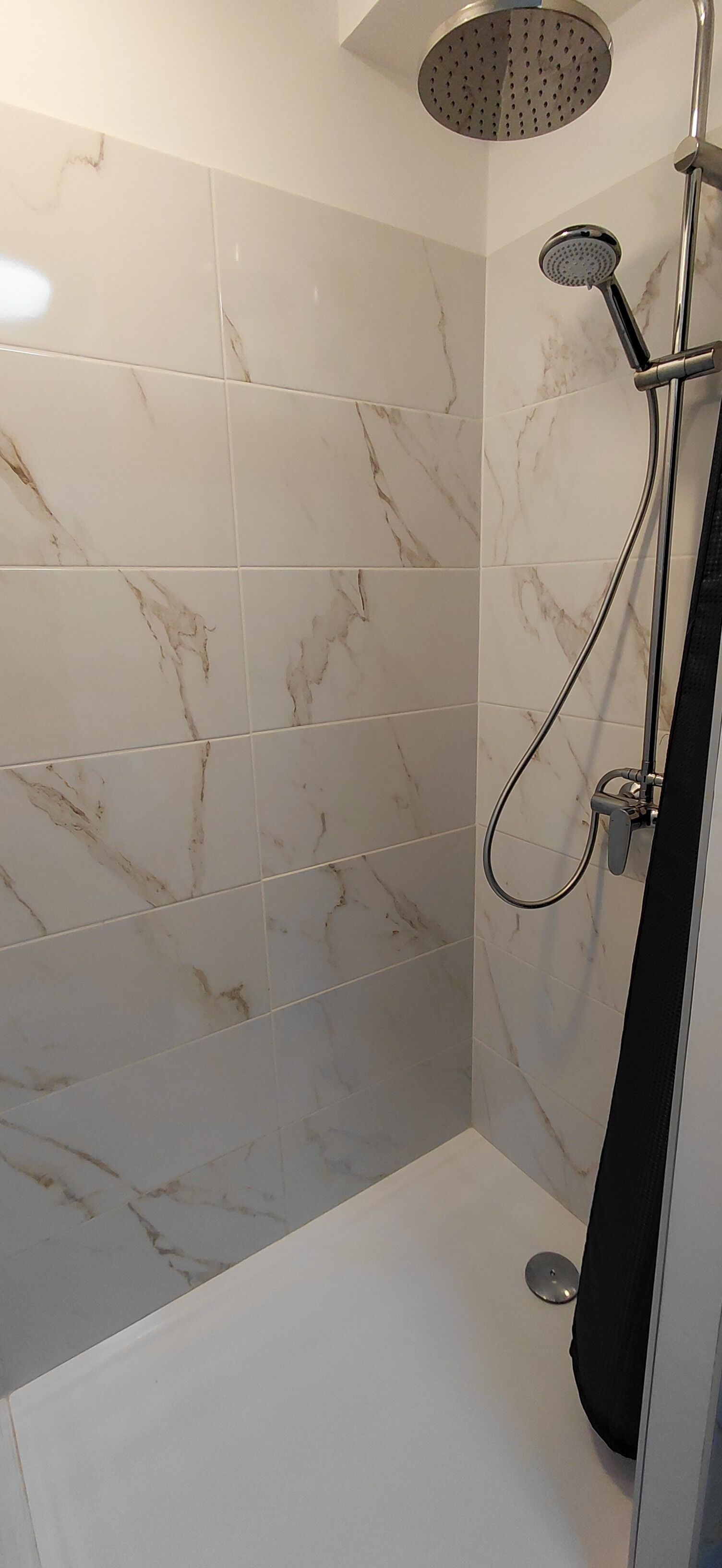 A shower with a handheld showerhead and a wall-mounted faucet.