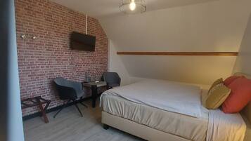 A bedroom with a brick wall, a bed with pillows, a desk with a chair, and a mounted TV.