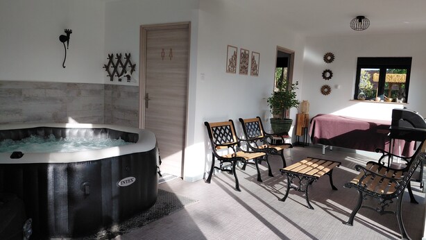 A room with a hot tub, two wooden chairs, a table, a bench, and a window with a view. - Villa Maëlla (Saint-Michel-Tubœuf)