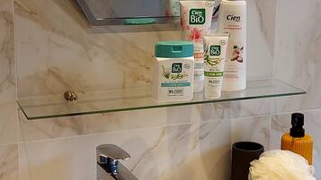 Un baño con un estante de vidrio que sostiene artículos de tocador, un lavamanos con un grifo moderno y un perchero sobre el espejo.