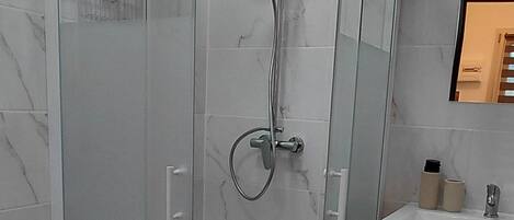 A modern bathroom with a glass-enclosed shower, a toilet, and a vanity with a mirror.