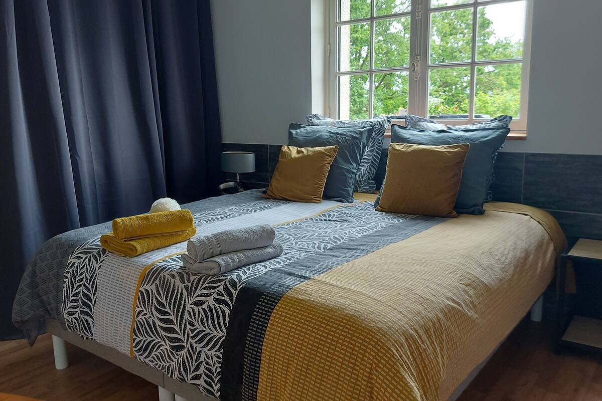 Un lit bien fait, avec une couvre-lit à motifs, deux oreillers et des serviettes enroulées.