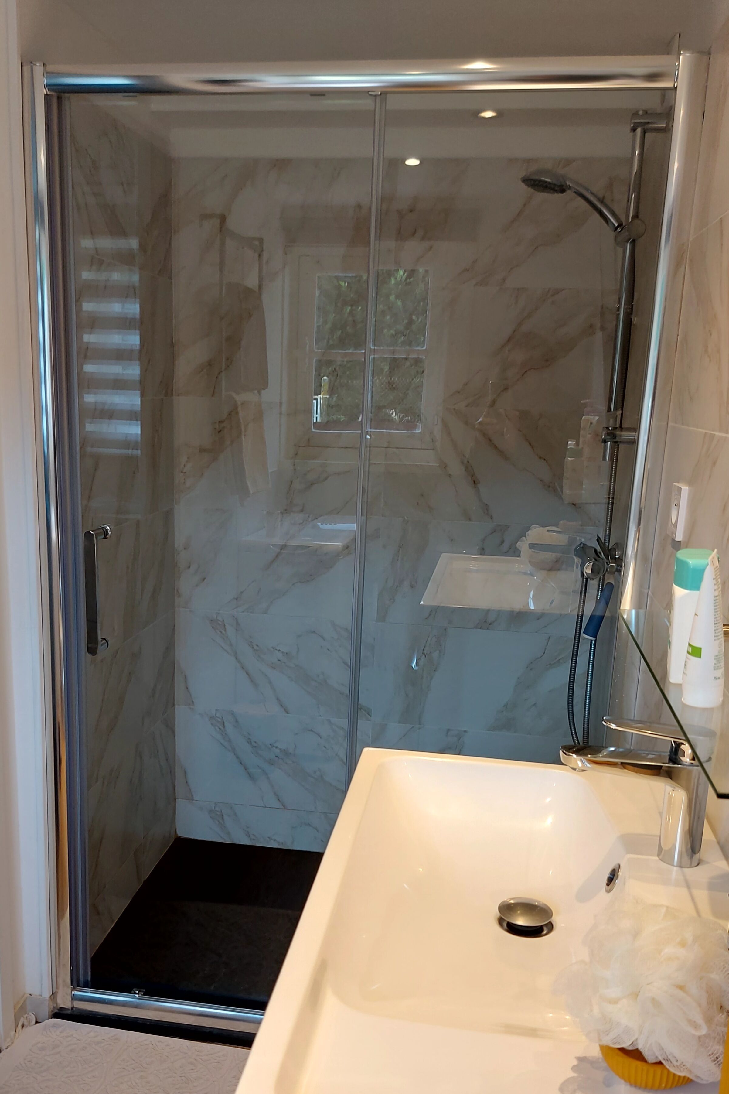Une salle de bain avec une douche à parois de verre, un lavabo blanc et un miroir.