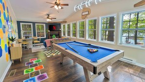 A pool table in a room with large windows, a ceiling fan, and a view of trees outside. - New Game Room-Snow Cones-Pet Friendly-Dock-Fire Pit-Kayaks-Paddleboards- (Martin)
