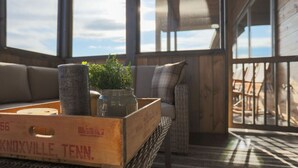 A cozy seating area with wicker furniture, a wooden crate with Knoxville, Tenn. text, and a planter with greenery. - Renewed Spirit 7 Bedroom Cabin with Heated Pool (Sevierville)