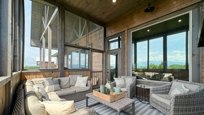 A spacious living area with wicker furniture, large windows, and a view of the outdoors. - Renewed Spirit 7 Bedroom Cabin with Heated Pool (Sevierville)